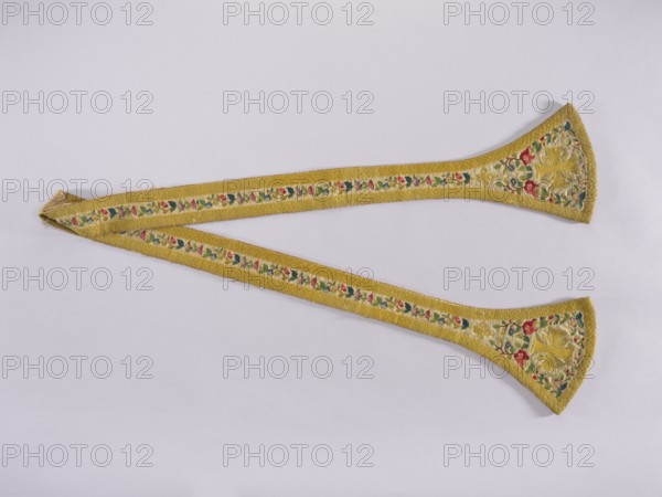 Stole, 18th century, Poland. Liturgical vestment, length 205 cm, width 22 cm. Made of woolen fabric with linen lining pink. Embroidered along the edges with floral tendrils; ends of the paddles embroidered with equal-armed crosses at the center. At the junction of the paddles and the waistband is an embroidered floral rosette motif. Around the edges is an embroidered band with a carp-scale motif imitating gold braid. Dominant ornament colors: white background, yellow, green, pink, and blue. Categories: church paraments, liturgical vestments, plant ornaments, sacred art, churches and chapels furnishings., A long fabric band laid flat on a pale background, with a yellow outer border and a lighter inner strip featuring a repeating floral pattern in red, pink, green, and blue; both ends widen into rounded triangular shapes with embroidered floral motifs and a central star-like design in yellow, with visible stitching and slight fraying at one end.