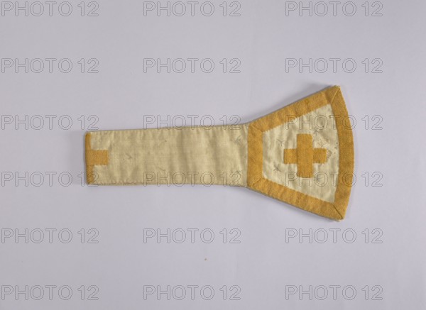 church paraments, liturgical vestments, sacred art, churches and chapels equipment. 18th century, Poland, liturgical vestment; height 83 cm, width 21 cm., A flat fabric object lies on a light gray background, shaped with a long rectangular stem widening into a trapezoidal head; the fabric shows a pale beige center with mustard yellow borders and appliqué shapes, and small pale blue stitched X-shaped marks on the wider section; the rectangular end has a mustard yellow tab, the wider end has a mustard yellow border and a central mustard yellow cross-like appliqué, with visible texture and slight wrinkles in the fabric.