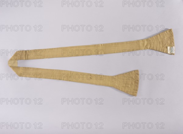 Stole, 18th century, Poland; liturgical vestment, embroidered, length 208 cm, width 18 cm. The item relates to church paraments, sacred art, and liturgical vestments; discusses form, symbolism, manufacturing techniques, and significance of embroidery in Polish religious tradition, including role of religious orders Warsaw Capuchins in shaping liturgical culture., A long, narrow fabric strip laid flat against a pale background, with a muted gold color and a slightly shiny, textured surface; the strip widens into flared ends with visible creases and stitch lines, and one end shows a small patch of lighter fabric; the background appears light gray or off-white.