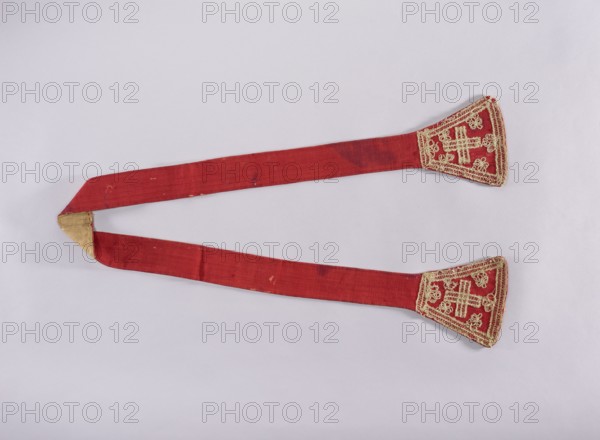 Stole, 18th century, Poland; liturgical vestment stole; length 184 cm, width 18 cm; church paraments, liturgical vestments, sacred art; churches and chapels equipment., A long red fabric band folded into a U shape with a triangular gold patch at the bend and ornate gold embroidery at each free end; the fabric shows some darker red stains and small worn spots, and the background is a pale light gray.