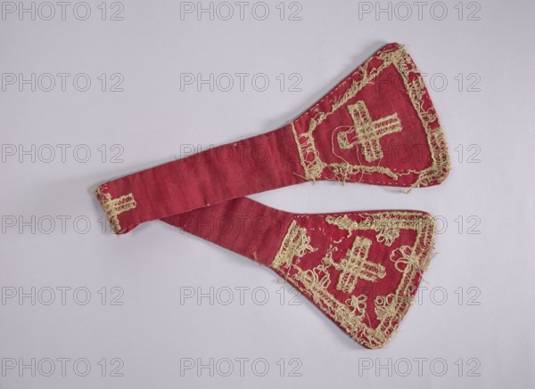 church paraments; liturgical vestments; sacred art; churches and chapels equipment. 18th century, Poland; liturgical vestment; length 84.5 cm; width 18 cm., A red fabric item with ornate beige embroidery laid flat on a pale gray background; the fabric forms two tapered sections joined at a wider end, each wide end shaped like a rounded triangle and decorated with intricate looped and stitched beige threadwork including cross-like motifs and border detailing, while the long connecting strip is plain red with small stitched accents and a small embroidered beige element at one narrow end; visible colors include red, beige, pale gray, and subtle darker red shading on the fabric.