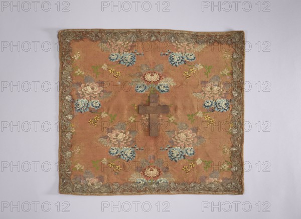 Velum; creator, Rómmel Jadwiga gift, provenance; church paraments; flowers, leaves, plant ornaments; sacred art; churches and chapels furnishings; 2nd half of the 18th century; France; liturgical parament; height 47 cm, width 53 cm, A square textile with a warm brown background decorated with a repeating floral pattern in shades of blue, pink, cream, green, and yellow, featuring several stylized blossoms and leafy sprigs; a wooden cross in a darker brown is placed near the center; the textile has an ornate border with metallic-looking trim in a silvery-gold tone and shows subtle variations in the brown ground where the fabric weaves and ages.