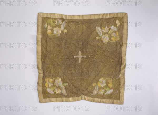 Velum, unknown author. Velum made of gold mesh fabric, embroidered with colorful silk threads in motifs of floral branches placed in the corners. Predominant colors: gold, blue, and silver. A cross made of narrow silver braid is sewn in the center. The edges are trimmed with gold braid. Blue silk lining. 18th century, Poland. Liturgical vestment. Height 48 cm, width 46 cm. Church vestments; floral ornaments; flowers; leaves; plant ornaments; sacred art; churches and chapels furnishings., A square textile with a gold-brown central field and a pale gold border, laid flat on a light gray background; the central area has a subtle net-like texture and a pale mark near the center forming a short cross shape; each corner of the textile shows a cluster of floral shapes in pale yellow, white, light green, and muted peach, with small pale green accents; the border is a slightly darker gold with a smooth sheen and the textile surface shows gentle wrinkles and creases.