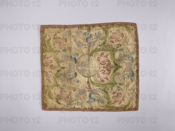 Velum;, liturgical parament church paraments; 18th century, France; sacred art; churches and chapels furnishings; flowers, leaves, plant ornaments; height 42.5 cm, width 48.5 cm., A square textile with a pale beige background laid flat on a light gray surface, showing an ornate embroidered pattern with a few curved leafy motifs in green, clusters of floral shapes in red and blue, and some pale gray embroidered elements; the fabric appears slightly wrinkled and worn, with a narrow decorative border in muted pink and gold tones around the edges.