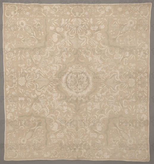 Cope, repossession provenance; clothing accessory; Henryków German: Heinrichau; In the cartouche there are two shields with the monograms CH and DL. Around it are flowers, leaves, and cartouches winding on long stems. Around the edges is a border with a floral tendril motif. Early 18th century, Saxony; fabrics; height 103 cm, width 96 cm, The image shows a large rectangular textile with an overall beige background and intricate off-white embroidered patterns; the design features a central circular medallion with ornate scrolls and laurel-like motifs, surrounded by a symmetrical arrangement of floral and foliate elements, curved vine-like shapes, shield-like forms, and scalloped panels; a decorative border runs along the edges with repeating floral motifs and small ornamental panels; the embroidery creates subtle raised texture and tonal contrast against the beige ground, and the colors visible are beige and off-white.