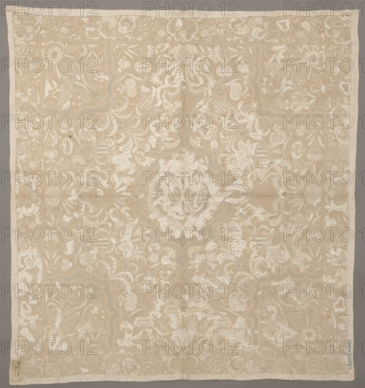 Cope, clothing accessory, In the cartouche there are two shields with the monograms CH and DL. Around it are flowers, leaves, and cartouches winding on long stems. Around the edges is a border with a floral tendril motif. Early 18th century, Saxony, fabrics, height 103 cm, width 96 cm, A square textile with a decorative floral and foliate pattern appears spread flat against a neutral background; the fabric shows an overall beige tone with lighter off-white motifs forming an intricate, symmetrical design of stylized flowers, leaves, and scrolling elements across the surface, with a narrow plain border in a slightly lighter beige running around the edges; the textile has subtle variations in beige and off-white shades, some areas showing slightly darker beige wear or shadowing, and there are small tags or labels attached near two corners that contrast with the fabric.