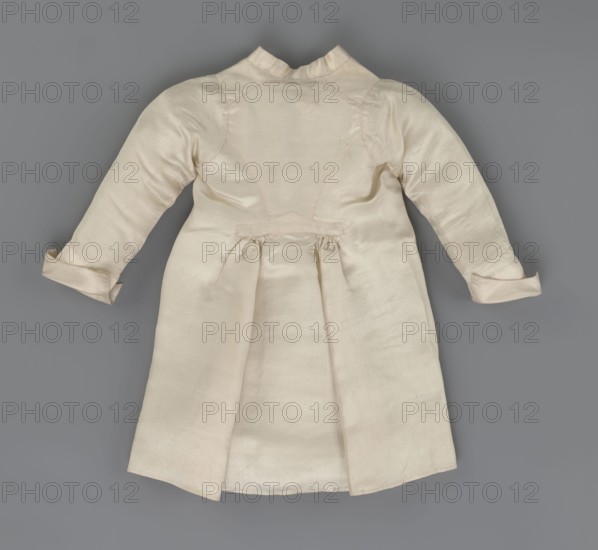 Children's dress made of cream satin. Long, fitted at the top, slightly flared at the bottom. Fastened at the front to the neck with 12 small, covered buttons. Low, stand-up collar. Long, set-in sleeves finished with turn-up cuffs. Widened at the back from waist level down by gathered pleats. Unaltered. 2nd half of the 18th century, Poland; garment; length 49 cm, width 100 cm bottom., A light cream-colored long-sleeved dress or coat laid flat against a medium gray background, showing the back with a high collar, fitted bodice seams, a gathered waist detail, turned-up cuffs, and a center pleat in the skirt area; visible colors include cream and gray.