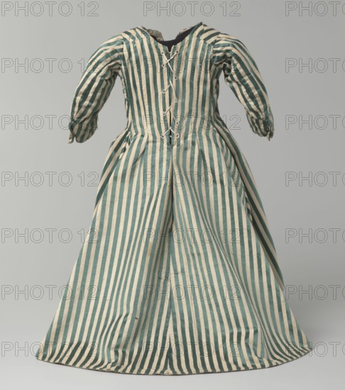 Children's dress, 18th century clothing, fashion. Children's dress made of satin with green and cream stripes. Fitted at the top, flared at the bottom, extended at the back by a semicircular train. Bodice is slit at the back and laced. Neckline is semicircular with a sharp V at center front. Long sleeves, cut in an arc at elbow height, finished with small close-fitting cuffs fastened with covered buttons. Lining made of white linen canvas. Unaltered. 18th/19th century, Silesia; length 49 cm., A striped dress displayed against a plain pale background, showing a fitted bodice with long sleeves and a full skirt; the fabric has alternating vertical stripes in teal and off-white, with visible seams and gatherings at the waist and a series of tied closures down the back of the bodice, and a dark inner lining seen at the neckline.