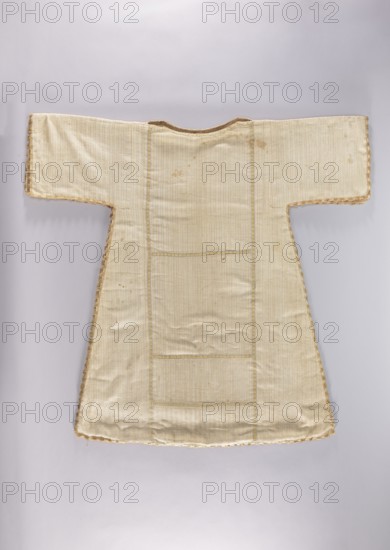 Dalmatic;, dalmatic with floral and leaf plant ornament motifs; liturgical vestment for church use; sacred art; churches and chapels furnishings; 2nd half of the 18th century; place of origin, dimensions: height 120 cm, width 85 cm alternative dimensions listed: height 110 cm, width 79 cm., A light-colored garment laid flat against a pale background, with a T-shaped silhouette and wide horizontal sleeves, made from a textured fabric with subtle vertical ribbing; the edges are trimmed with a scalloped decorative border in a slightly darker beige or golden tone, and there are a few small darker stains and spots on the front; overall colors visible are cream, beige, pale gold, and light tan.