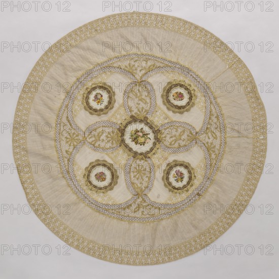 Doily, unknown creator; round doily sewn from two pieces of machine lace, bobbin lace, and fabric with colorful petit point embroidery. Five medallions arranged in the central circle, each surrounded by bobbin lace, with four oval lace medallions with floral branches between the medallions. Mid-19th century, Europe. Fabric, lace. Diameter 115 cm., A circular textile with a central round medallion surrounded by a decorative ring and an outer border, featuring a pale beige main background with gold embroidery and trim, a few scalloped circular appliqués each containing small floral motifs in pink, red, yellow, and green, several interlacing gold embroidered bands forming petal-like shapes, and areas of cream and off-white fabric textures; the outer rim shows a patterned gold lace-like band against the beige, and the overall piece displays a mix of subtle beige, cream, gold, pink, red, yellow, and green colors.