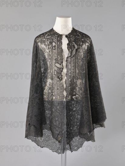 Cape - mantilla;, shawl; purchase provenance; fashion; women's clothing; clothing accessory; lace mantilla cape, triangular. Pattern: garlands of leaves at the bottom, conical trees in the bends at the bottom. Late 19th century, France. Lace; dimensions: length 96 cm, width 344 cm., A sheer black lace cape displayed on a white mannequin bust against a neutral gray background, featuring ornate floral and scroll-like lace patterns, scalloped edges along the hem and front opening, a high rounded neckline, and a central front opening with delicate ruffled trims; the lace shows varying densities and transparent areas, with the black lace contrasting against the white of the mannequin and the gray backdrop.