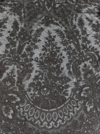Cape - mantilla; creator, shawl; purchase provenance; fashion; women's clothing; clothing accessory; lace mantilla cape; triangular shape. Pattern: garlands of leaves at the bottom, conical trees in the bends at the bottom. Late 19th century, France. Clothing accessory. Dimensions: length 96 cm, width 344 cm., A close-up of a patterned textile showing an intricate floral and ornamental design in dark gray thread against a lighter gray sheer background, featuring a group of stylized flowers and leaves arranged within oval and scroll-like shapes, with delicate netting visible beneath, and several areas where the dark embroidered motifs form repeating leafy sprays and rounded decorative borders.