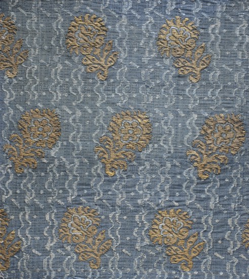 Fabric fragment, lamé fabric, fragments of silk fabrics, patterned fabrics, silk fabrics, fabrics with preserved reports, floral patterns, Italian fabrics. Color: blue background, brocaded with metal thread. Report: 14.5 x 6.5. LISERE BASE, BOARDED AND BOOKLETED Construction: Weft grosgrain background with a blue silk warp and a silk weft with a bundle of blue and white threads. Liseré technique with the basic weft. A prominent drawn gold plate – lamella – is attached to every fourth weft thread. Brooching thread with a loose braid of gold plate on a yellow silk base. Design: Report - length 13 cm, width 6.5 cm. Blue background with finely wavy lines shimmering in shades of blue and white running along the length of the fabric. Against this background, small floral projections single calyxes on short leafy stems in two similar forms, arranged in rows, shifted by half a repeat and facing right or left. 1st half of the 17th century, Italy; fabrics, height 78.5 cm, width 23.5 cm., A woven...