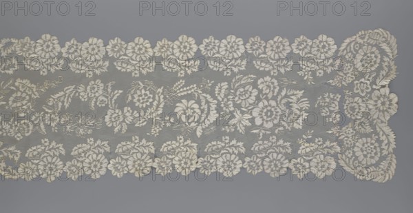 Shawl, shawl, clothing accessory, women's clothing, fashion, lace with serrated edges, design of twigs with two flowers in the bends and curling flower twigs in the middle part, 19th century, Europe, length 48 cm, width 260 cm, A rectangular piece of lace displayed against a gray background, showing an intricate floral pattern with a scalloped edge on two opposite sides; the lace is primarily off-white or cream, with delicate embroidered flowers and leaves forming repeating motifs across the sheer netting, and several larger floral clusters and curved leaf sprays concentrated toward one end, while smaller flower motifs create a border along the top and bottom edges.