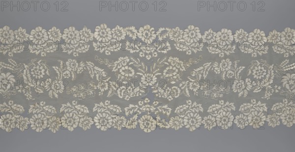 Shawl, shawl; purchase provenance; clothing accessory; women's clothing; fashion; lace with serrated edges; design includes twigs with two flowers in the bends and curling flower twigs in the middle part; 19th century, Europe; length 48 cm, width 260 cm., A wide horizontal piece of lace with a repeated floral pattern in off-white and cream tones set against a muted gray background, featuring a scalloped top and bottom edge formed by clusters of embroidered flowers, leaves, and curling vines, with several larger rosette-like blossoms and a group of smaller filler flowers and foliage arranged symmetrically across the fabric, the lace showing variations in texture where the dense embroidery contrasts with the finer netted sections, and a few tiny irregularities in the thread color and weave.