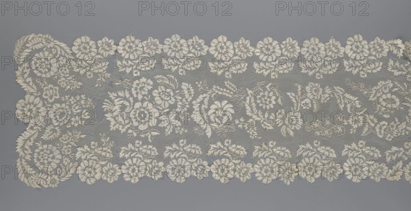 Shawl, 19th century, Europe. Lace shawl, women's clothing accessory; serrated edges; design: in the bends twigs with two flowers, middle part with curling flower twigs. Length 48 cm, width 260 cm., A wide piece of lace fabric laid flat, showing an intricate floral pattern with scalloped edges; the lace features a group of large and small flower motifs, leafy tendrils, and swirling vine shapes arranged in horizontal bands with repeating clusters; the background netting is fine and sheer, while the embroidered elements are raised and textured; visible colors include off-white or cream for the lace and a muted gray background.