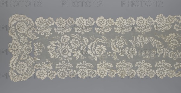 Shawl; creator, shawl; clothing accessory; women's clothing; fashion; lace with serrated edges; design includes twigs with two flowers in the bends and curling flower twigs in the central area; 19th century, Europe; length 48 cm; width 260 cm., A long strip of lace with an intricate floral pattern lies against a solid background; the lace features a repeating arrangement of stylized flowers, leaves, and curling tendrils in an off-white or cream color, with delicate openwork and denser embroidered sections creating texture, while the background appears as a uniform medium gray.