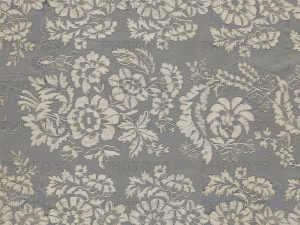 Shawl, shawl, clothing accessory, women's clothing, fashion, lace with serrated edges; design includes twigs with two flowers in the bends and curling flower twigs in the middle part. 19th century, Europe. Length 48 cm, width 260 cm., The image shows a delicate lace fabric with a repeating floral pattern in off-white against a muted gray background, featuring a few large stylized flowers, several leafy sprigs, and a group of vine-like tendrils, all rendered in textured embroidery with visible netting between motifs.