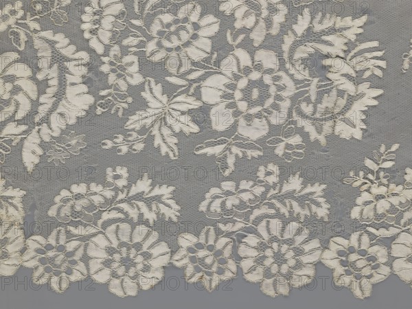 Shawl, shawl; 19th century, Europe; clothing accessory for women; lace with serrated edges; decorative design: in the bends twigs with two flowers, in the middle part curling flower twigs; dimensions: length 48 cm, width 260 cm., A piece of lace fabric with an intricate floral pattern in shades of off-white and cream on a gray background, showing a mesh-like net base with embroidered flowers, leaves, and scroll motifs, scalloped edges along one side, and areas where the lace overlays the background creating subtle shadows and varying texture.