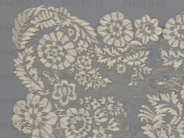 Shawl, shawl, clothing accessory, women's clothing, fashion; lace with serrated edges; design: in the bends twigs with two flowers, central area with curling flower twigs; 19th century, Europe; dimensions: length 48 cm, width 260 cm., A delicate piece of off-white lace with an intricate floral pattern lies against a flat gray background; the lace shows a variety of stylized flowers and leaves connected by a fine netting, with scalloped edges and some frayed threads and small gaps where the netting is worn. The visible colors are off-white and gray.