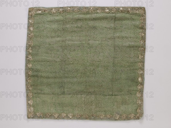 Velum fragment; maker, churches and chapels equipment; repossession provenance; church paraments; 18th century, France; liturgical parament; fabric; height 52 cm, width 54 cm, A roughly square piece of fabric in a muted green shade fills most of the image, with a worn, slightly wrinkled surface and a subtle woven floral or foliage pattern visible across it; the fabric is bordered on all sides by an ornate trim in metallic gold tones that forms a repeating scallop-like motif, and a hint of pale blue fabric is visible along the outer edge beneath the trim; the background around the fabric is a very light neutral color.
