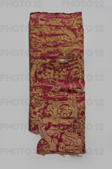 Fabric fragment, fragments of silk fabrics, patterned brocade with preserved selvedge and drawn thread. Fragment of a brocade with a large repeat, probably a net composition, with stylized plant motifs pomegranate. Brocaded with gold thread in an S braid on a yellow silk core fringed, augmented with drawn gold thread. Colors: cherry red background, yellow and gold ornament. Cherry warp, yellow, gold and natural-colored silk wefts raw silk weft. Green selvedge. Pattern drawing difficult to read due to worn brocades and background wear. Selection width: 0.4–0.5 cm. 16th century, Spain, height 71.5 cm, width 27.5 cm., A worn rectangular textile with frayed edges displayed against a light gray background, showing a pattern of raised decorative shapes in a muted gold color over a faded deep red ground, with areas where the red fibers are disturbed and small holes reveal lighter threads beneath, the fabric surface appearing textured and uneven with loose threads and a few small tears, and th...