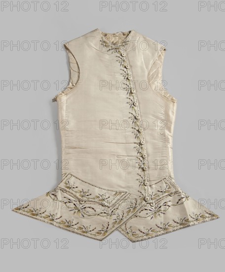 Vest, plant motifs, garlands ornament; men's clothing, 18th century, embroidery, waistcoat. Men's waistcoat of cream silk, embroidered. Straight cut, without a collar; trapezoidally cut hems; low-set pockets covered with flaps. Fastened to the neck with 12 covered and embroidered buttons; identical buttons under the pocket flaps. Embroidery decorates the edges at the closure, the pocket flaps, and the flaps under the pockets. Small floral garlands and tied bundles of grass. Embroidery with satin stitch. Predominant colors: yellow, green, and dark purple. Laced back, silk lining. Fabric-covered and embroidered buttons. 1780s, Europe; Silesia. Garment; length 70 cm., A sleeveless, light beige silk garment laid flat against a pale gray background, showing a high neckline and an asymmetrical front opening with a row of covered buttons; the fabric has a subtle sheen with visible creases and seams, and ornate floral embroidery along the front opening and hem in shades of green, gold, brown, ...