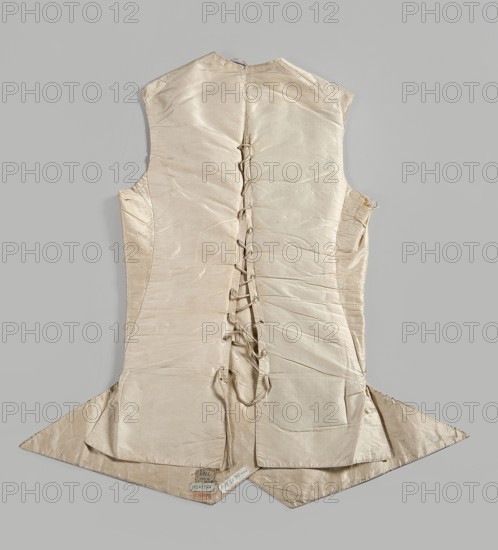 Vest, repossession provenance; plant motifs; garlands; Henryków German: Heinrichau — museum repository; clothing, men's clothing, 18th century; embroidery; waistcoats. Men's waistcoat of cream silk, embroidered. Straight cut, without a collar; trapezoidally cut hems; low-set pockets covered with flaps. Fastened to the neck with 12 covered and embroidered buttons; identical buttons under the pocket flaps. Embroidery decorates the edges at the closure, the pocket flaps, and the flaps under the pockets. Small floral garlands and tied bundles of grass. Embroidery with satin stitch. Predominant colors: yellow, green, and dark purple. Laced back, silk lining. Fabric-covered and embroidered buttons. 1780s, Europe; Silesia. Garment, length 70 cm., A sleeveless garment laid flat on a neutral grey background, made of a shiny light beige or ivory fabric with visible seams and darting, featuring a central back opening with a series of fabric loops and ties running vertically, a fitted waist that f...
