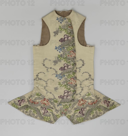 Vest, floral and plant ornaments, patterned fabrics. Predominant ornamental colors: silver, plum, green, and raspberry. Front of brocaded silk fabric with motifs arranged around the edges. Fastened with 12 buttons embroidered with gold threads. No collar. Side flaps with flapped pockets, three buttons under the flaps as for the closure. Back: bottom and sides of fabric as on the front, but the cut-out pieces are plain without brocade. Cream silk lining. 1740–1760, England fabric possibly, Silesia. Garment, length 74 cm., A sleeveless garment laid flat on a pale gray background, made from a cream-colored fabric with a central vertical panel of floral embroidery; the embroidery features a scrolling arrangement of leaves and flowers in shades of green, purple, blue, red, and gray, with silver-gray foliage motifs woven throughout. The garment has a high rounded neckline, deep arm openings revealing a brown inner lining, and a flared skirt-like peplum at the bottom with pointed sides that c...
