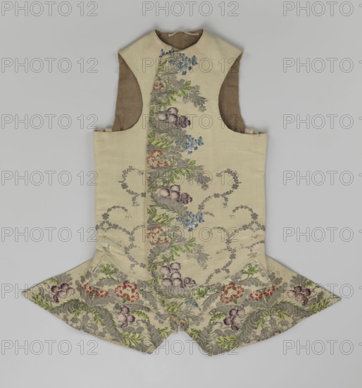Vest, floral and plant ornaments, patterned brocaded silk fabric front, predominant ornamental colors: silver, plum, green, and raspberry. Motifs arranged around the edges. Fastened with 12 buttons embroidered with gold thread. No collar. Side flaps with flapped pockets; three buttons under the flaps as closures. Back: bottom and sides of fabric match front, cut-out pieces plain without brocade. Cream silk lining. Dated 1740–1760. Origin: England fabric possibly, Silesia. Garment, length 74 cm., A sleeveless garment laid flat against a light gray background, made from a pale cream fabric with a central vertical panel of floral embroidery running from the neck to the hem, flaring into a skirt-like pointed bottom; the embroidery shows a mix of floral sprigs and leafy fronds in colors including green, purple, blue, red, and gray, with additional gray scrolling motifs on the cream areas; the armholes reveal a brown inner lining and the garment has a rounded neckline and tailored seams.