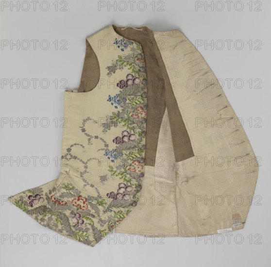 Vest, floral and plant ornaments, patterned brocaded silk fabric. Predominant ornamental colors: silver, plum, green, and raspberry. Front of brocaded silk fabric with motifs arranged around the edges. Fastened with 12 buttons embroidered with gold threads. No collar. Side flaps with flapped pockets; three buttons under the flaps as for the closure. Back: bottom and sides of fabric as on the front, but the cut-out pieces are plain without brocade. Cream silk lining. 1740–1760, England fabric?, Silesia, garment, length 74 cm., A sleeveless garment laid flat with an outer layer in a pale cream color decorated with a floral woven pattern in green, purple, blue, and red, showing leafy and flower motifs along one side and hem, and an inner lining in shades of beige and light brown with visible seams and worn areas.