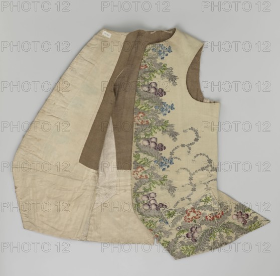 Vest, floral and plant ornaments; patterned brocaded silk fabric front with motifs arranged around the edges; predominant ornamental colors: silver, plum, green, and raspberry; fastened with 12 buttons embroidered with gold thread; no collar; side flaps with flapped pockets and three buttons under the flaps for closure; back: bottom and sides of fabric like the front, but cut-out pieces plain without brocade; cream silk lining; garment vest, length 74 cm; dated 1740–1760; probable origins: England fabric? and Silesia., A sleeveless garment laid flat showing an outer patterned panel and an inner plain lining, with the outer fabric in a light cream color decorated with a vertical floral border featuring flowers and foliage in green, blue, purple, pink, red, and gray tones, and areas of gray scrollwork; the lining is predominantly off-white and beige with a brown inner facing strip, and the garment shows seams, folds, and the armhole opening against a neutral light gray background.