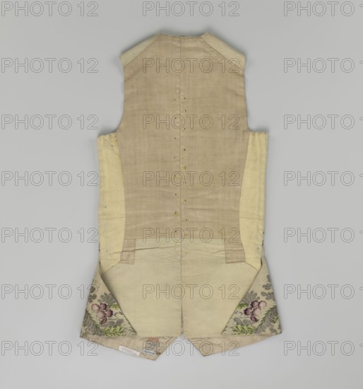 Vest, floral and plant ornaments, patterned brocaded silk fabric. Predominant ornamental colors: silver, plum, green, and raspberry. Front of brocaded silk fabric with motifs arranged around the edges. Fastened with 12 buttons embroidered with gold thread. No collar. Side flaps with flapped pockets, three buttons under the flaps as for the closure. Back: bottom and sides of fabric as on the front, but the cut-out pieces are plain without brocade. Cream silk lining. 1740–1760, England fabric ?, Silesia. Garment, length 74 cm., A sleeveless garment laid flat viewed from the back, made of pale beige and cream fabrics with a central panel of slightly darker beige and lighter cream side panels, featuring a vertical row of small buttonholes down the middle back, a short split at the bottom center, and a few internal seams and stitch lines visible. The lower corners of the garment fold outward to reveal triangular patterned fabric inserts with floral motifs in shades of green, purple, and pin...