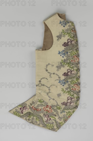 Vest, floral and plant ornaments, patterned brocaded silk fabric with predominant ornamental colors silver, plum, green, and raspberry. Front motifs arranged around the edges. Fastened with 12 buttons embroidered with gold threads. No collar. Side flaps with flapped pockets, three buttons under the flaps as for the closure. Back: bottom and sides of fabric match front, but cut-out pieces are plain without brocade. Cream silk lining. 1740–1760, England fabric possibly, Silesia, garment, length 74 cm., A single sleeveless garment piece laid flat, made of a light cream fabric with a visible brown inner lining at the armhole, decorated with a woven floral and foliate pattern along one side and the lower flap; the embroidery shows flowers and leaves in colors including green, purple, blue, red, and grey, with a row of fabric-covered buttons along the decorated edge and grey leafy vine motifs scattered on the plain areas.