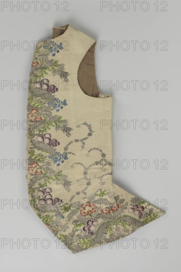 Vest, floral and plant ornaments, patterned fabrics. Predominant ornamental colors: silver, plum, green, and raspberry. Front of brocaded silk fabric with motifs arranged around the edges. Fastened with 12 buttons embroidered with gold thread. No collar. Side flaps with flapped pockets, three buttons under the flaps as for the closure. Back: bottom and sides of fabric as on the front, but the cut-out pieces are plain without brocade. Cream silk lining. Dated 1740–1760. Origin: England, and Silesia. Garment, length 74 cm., A single sleeveless garment laid flat showing an off-white or beige fabric with an embroidered floral border along one edge featuring a mix of colors including green leaves, purple and mauve blossoms, blue flowers, and orange-red blooms, with additional grayish foliate scrollwork woven into the background; the garment has a rounded armhole revealing an inner lining in a brownish tan tone and a pointed extension at one end that displays the same floral pattern and a fe...