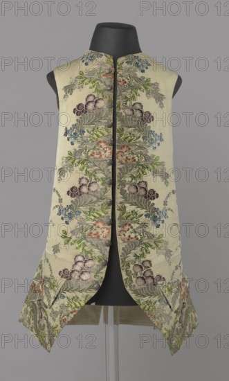 Vest, repossession provenance. Floral and plant ornaments on patterned brocaded silk fabric; predominant colors silver, plum, green, and raspberry. Front motifs arranged around the edges. Fastened with 12 buttons embroidered with gold threads. No collar. Side flaps with flapped pockets; three buttons under the flaps for closure. Back: bottom and sides patterned as on the front, but cut-out pieces plain without brocade. Cream silk lining. Dated 1740–1760. Likely England fabric? and Silesia origin. Garment; length 74 cm., A sleeveless waistcoat displayed on a black mannequin torso against a gray background, made of a light cream fabric with an allover embroidered floral pattern; the embroidery shows a repeating vertical arrangement of stylized leaves and clusters of flowers in shades of green, muted blue, soft purple, pale pink, and warm coral, with silvery gray foliage and highlights; the garment has a high collar, a central front opening with a row of round fabric-covered buttons, and ...