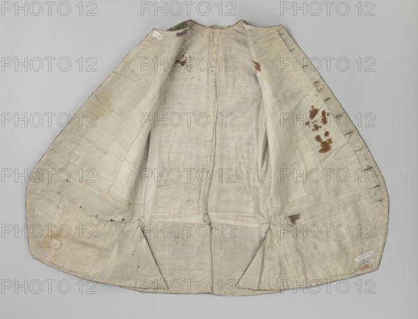 Vest, floral ornaments, patterned fabrics, Fastened to the neck with 11 buttons. Flaps on the sides, below them 4 buttons as for the fastening, embroidered in gold. The back is made of brown canvas at the top and fabric at the bottom as on the front. 1750s, Silesia, garment, length 76 cm, An open garment lining laid flat against a light gray background, showing an off-white and cream fabric with a few brown stains and patches, some darker brown spots along one side, several areas of visible stitching and seam lines, a few rectangular patched repairs, and subtle variations of beige and pale gray in the woven texture.