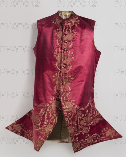 Men's vest made of cherry satin, embroidered. Straight cut, without sleeves or collar. Diagonal hemline, side pockets covered with large flaps, three covered buttons under each flap. Fastened to the neck with 11 covered and embroidered buttons. Circa 1740–1770, Silesia. Length 78 cm., repossession, Floral ornaments., A sleeveless garment displayed against a pale background, made of a shiny deep red fabric with a vertical panel of intricate gold embroidery running down the center and expanding into ornate floral and leafy patterns toward the lower flared sections, featuring decorative fabric-covered buttons along the front panel, a rounded high collar with matching embroidery, and a contrasting lighter-colored inner lining visible where the front splits; visible colors include deep red, gold, a light beige inner lining, and the pale neutral background.