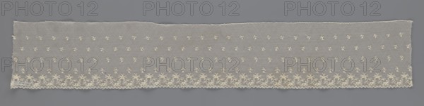 Fragment of lace, lace, unknown origin, floral ornaments, 19th century, Europe, lace, width 13 cm, length 75 cm, A long rectangular piece of delicate lace laid flat against a solid background, showing a translucent mesh with a repeating pattern of small floral motifs across most of its surface and a denser scalloped floral border along one long edge; the lace is a creamy off-white color with subtle variations in tone, and the background is a muted gray that contrasts with the lace.