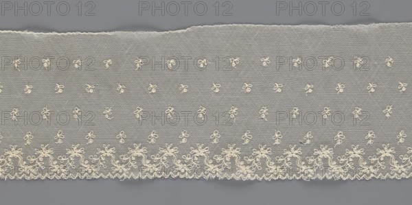 Fragment of lace, floral ornaments, 19th century, Europe, lace, width 13 cm, length 75 cm, A length of sheer fabric with a fine hexagonal mesh in pale cream laid against a gray background, featuring a repeating pattern of small embroidered bow-like motifs scattered across the main area and a denser embroidered border along one edge with flowing floral and scroll elements and a scalloped outer rim; the fabric shows a torn irregular top edge and a straight scalloped bottom edge, and the visible colors are cream and gray.