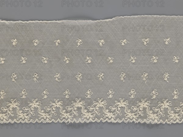Fragment of lace, lace, unknown origin, floral ornaments, 19th century, Europe, lace, width 13 cm, length 75 cm, A length of delicate lace fabric with an off-white or cream color laid against a gray background, featuring a hexagonal netting pattern overall, scattered small embroidered floral or bow-like motifs across the central area, and a denser embroidered scalloped border along the lower edge with flowing vine and flower shapes; the top edge shows a slightly frayed finish.