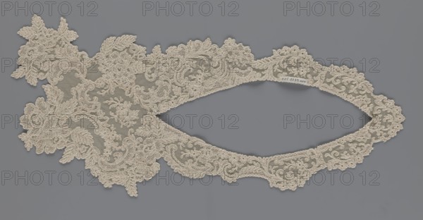 Collar, origin unknown, floral ornaments, clothing accessory for women's clothing, fashion, embroidery; connected at the bottom by a wide, irregular inset; 2nd half of the 19th century, Europe; width 19 cm, length 50 cm, A delicate piece of lace with an intricate floral and leaf pattern rests against a flat background; the lace is a light beige color with fine netting and raised embroidered motifs forming scrolling flowers and leaves, and the background is a muted gray.