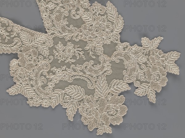 Collar, origin unknown, floral ornaments, clothing accessory for women's clothing, fashion, embroidery. Connected at the bottom by a wide, irregular inset. 2nd half of the 19th century, Europe. Width 19 cm, length 50 cm., A piece of lace fabric with an intricate floral and leaf pattern laid on a smooth background; the lace shows delicate netting and raised embroidered motifs including flowers, curling vines, and feathery leaves, with scalloped edges and ornate swirls; the lace appears in a light beige color and the background is a medium gray, creating visible contrast between the lace and its backdrop.