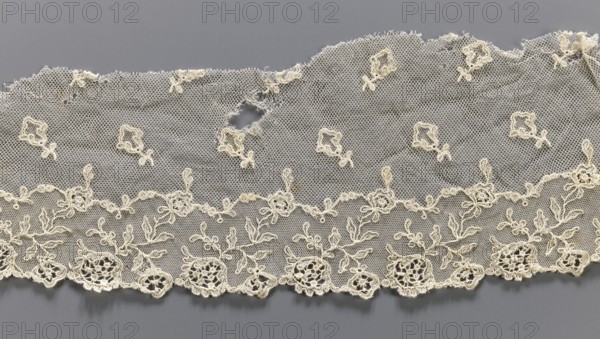 Lace fragment, lace, plant ornaments, tulle embroidered with twig and floral motifs around the lower edge and projections of small twigs above; upper edge cut off, unsecured. 19th century, Europe. Lace, width 12 cm, length 56 cm., A length of delicate lace fabric laid flat against a smooth background, showing a fine net ground with embroidered floral motifs and scalloped lower edge; the lace displays a few areas with small holes and frayed edges, and several raised embroidered flower and leaf designs connected by looping stems; the visible colors are off-white for the lace and a cool medium gray for the background.