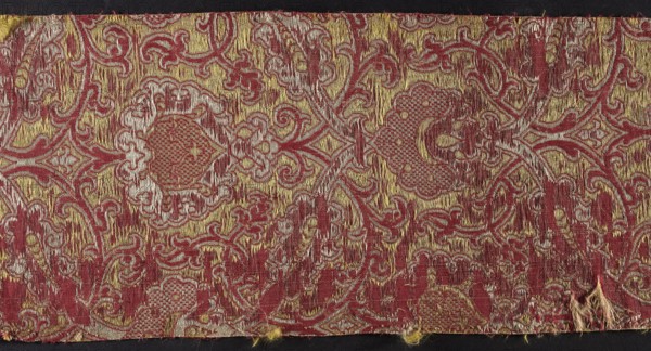 Fabric fragment, textiles, fragments of silk fabrics, patterned fabrics, brocades, net patterns. Brocade a two-warp, multi-thread fabric with a stripe structure in yellow background, dark red, and white pattern. The warp and the main weft shape intertwine in a satin weave. The binding warp binds the leading threads in a weft weave. Two drawn threads pass in a single course. Net composition. The pattern is created by two overlapping systems of white and red tendrils, creating net meshes in the form of pointed ovals. In the spaces between the intersecting systems of tendrils are woven palmettes, in places filled with a checkerboard of small ornaments. Report: 41.5 x width ? Colors: dark red cherry background, white, yellow, and silver drawn thread highlights. From a technical point of view, due to the use of a thick untwisted silk weft and due to the decorative motifs and the scale of the report, certain fabric fragments form one group and were probably created simultaneously and in the ...