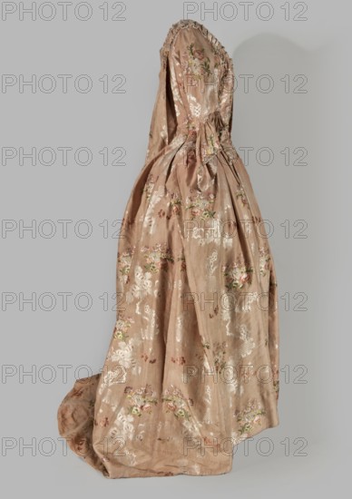 Two-piece robe à la française dress made of silk in the colour of dried rose with motifs of colourful flower bouquets and winding white lace ribbons. Overskirt manteau open at the front, with a triple pleat extending almost the entire width of the back that flows into a train. Bodice on linen lace with boning, laced at the front; deep, square neckline. Narrow, elbow-length set-in sleeves trimmed with ruffles of the same fabric. Neckline and bodice edges trimmed with a pleated ruffle decorated with multicolored cord trimmings twisted into tiny flowers. No lining. Skirt gathered with symmetrical pleats, spread out to the sides. Patterned fabric with floral ornaments, ribbons and ruffle decoration. Fabric report: height 24.5 cm, width 48.5 cm; width of fabric piece 54 cm. Dated c. 1760–1765; Silesia; possible origin France. Length 158 cm., A long historical-style dress displayed on a mannequin, shown from a side angle, made of a shiny pale brown fabric with a floral woven pattern; the dre...