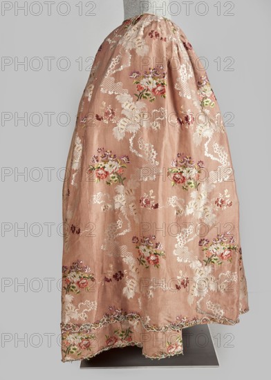 Robe à la française dress, floral ornaments, ribbon, flower bouquets, robe à la française, ruffles, clothing, women's clothing/fashion, patterned fabrics, 18th century. Two-piece dress made of silk in the colour of dried rose with motifs of colourful flower bouquets and winding ribbons of white lace. The overskirt manteau is open at the front, with a triple pleat extending almost the entire width of the back, flowing into a train. The bodice is on linen lace with boning, laced at the front. The neckline is deep and square. Narrow, elbow-length set-in sleeves trimmed with ruffles of the same fabric. Neckline and bodice edges trimmed with a pleated ruffle, decorated with multicolored cord trimmings twisted into tiny flowers. No lining. The skirt is gathered with symmetrical pleats, spread out to the sides. Fabric sample: height 24.5 cm, width 48.5 cm; width of fabric piece 54 cm. Date: 1760–1765. Place associated: Silesia; possible origin: France. Length 158 cm., A long skirt displayed o...