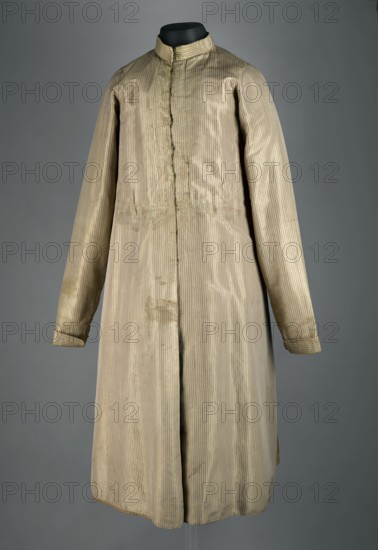 Zupan, noted. Polish clothing; painter Franciszek Teodor Eysmond 1859–1931 associated. Geometric ornaments; men's fashion, national costume. Long zupan, fitted at the top, flared at the bottom. Fastened with hooks and eyes to the neck, concealed fastening. Low stand-up collar. Long set-in tapered sleeves with turn-up cuffs, slit at the bottom and fastened with hooks and eyes. Back cut like a kontusz with a central column of fabric, widened from the waist by semi-flared pleats, adjustable at the top with ribbons. Pockets in the side seams. Silk satin with pearl-brown stripes. Back and lining of gray linen canvas. Hand-sewn. 18th/19th century, Poland. Length 118 cm; bottom circumference 243 cm., A long, light-colored striped coat displayed on a black mannequin neck, with a high collar and long sleeves; the coat shows subtle vertical stripes in beige and off-white tones, with areas of slightly darker discoloration and faint stains; the sleeves have small turned cuffs, and the front has a ...