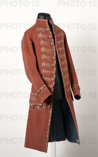Habit à la française. Habit of pink cloth, embroidered with motifs imitating braiding, miniature bouquets and garlands. Fitted at the top, widened at the back from the waist down with two slit pleats. Straight-cut tails. Fastened at the front with hooks and eyes; along the edge of the right tail are ten embroidered buttons imitating a fastener. Similar buttons: three on the cuffs, under the pocket flaps, and two on the back, at the top of the pleats, and two inside them. Long, set-in, narrow sleeves, cut in an arc at elbow height, finished with cuffs. Low, stand-up collar. Edges decorated with embroidery. Buttons covered with fabric and embroidered. Embroidery with unspun silk yarn in white, blue, and green. Fustian lining. Hand-sewn. 2nd half of the 18th century. Silesia. Garment. Length 103 cm., Repossession provenance. Flower bouquets, garlands, flowers ornament. Men's clothing; men's fashion; tailcoats; 18th century clothing., A long coat displayed on a black mannequin torso with a...
