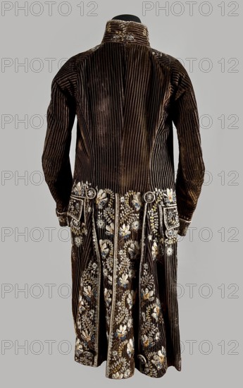 Habit à la française, tailcoat, floral ornaments, clothing, men's clothing, men's fashion, 18th century clothing. Habit of striped brown velvet, embroidered with fanciful flowers with large stamens and ears of grass. Fitted at the top, widened by pleats at the bottom, at the back, from the waist down. Long, set-in sleeves, cut in an arc at elbow height, finished with cuffs. Fastened with buttons, the skirts are cut in an arc, overlapping at the chest. Embroidery along the edges of the pockets, on the cuffs, pocket flaps, collar, and back pleats. The back is cut with a center seam; the back pleats do not overlap. Three buttons under the pocket flaps and on the cuffs. 1780s, Silesia, garment, length 111 cm, A long, dark brown velvet coat with vertical ribbing visible across the back and sleeves, shown from the rear on a neutral gray background; the lower portion of the coat is decorated with detailed floral embroidery in colors including white, light blue, gold, and pale yellow, with add...